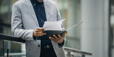 Man in a suite holding a folder with paper.